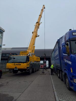 Yellow Mobile Crane Hoisting Operation Near Blue Truck on Industrial Site